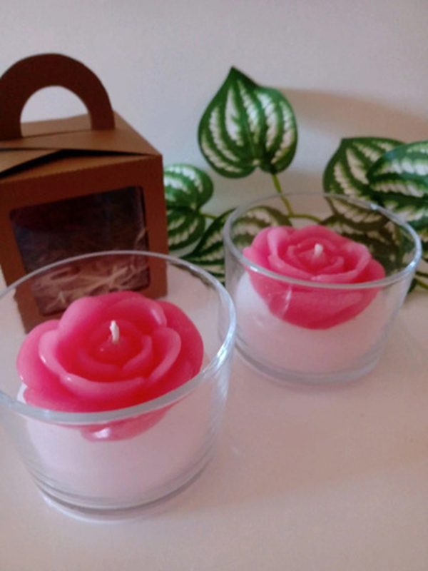 Velas artesanales con forma de rosa en vasitos de vidrio, en tonos coral y rosa.