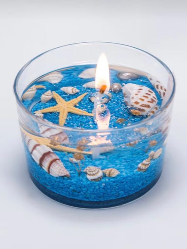 Vela artesanal tipo océano en vaso, con gel azul, conchas y estrella de mar.