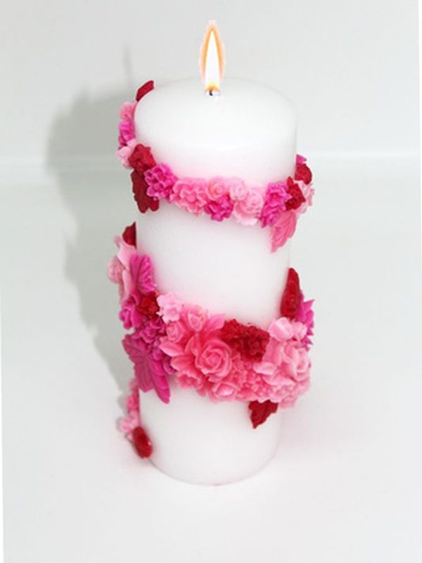 Vela artesanal tipo cirio blanca decorada con flores rosadas.