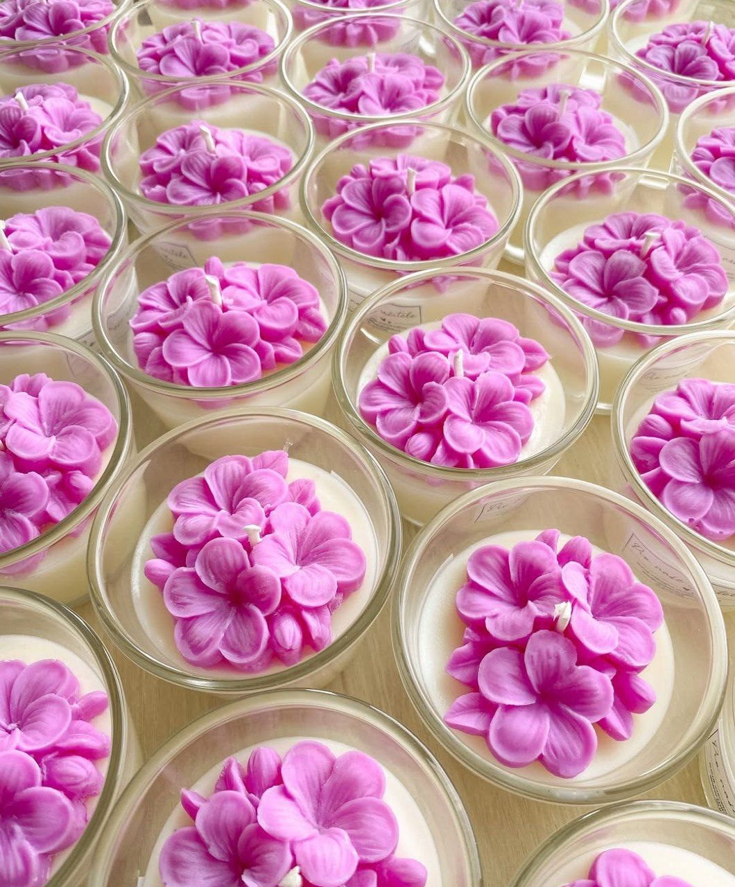 Velas artesanales con flores rosadas en vasitos, hechas a mano.