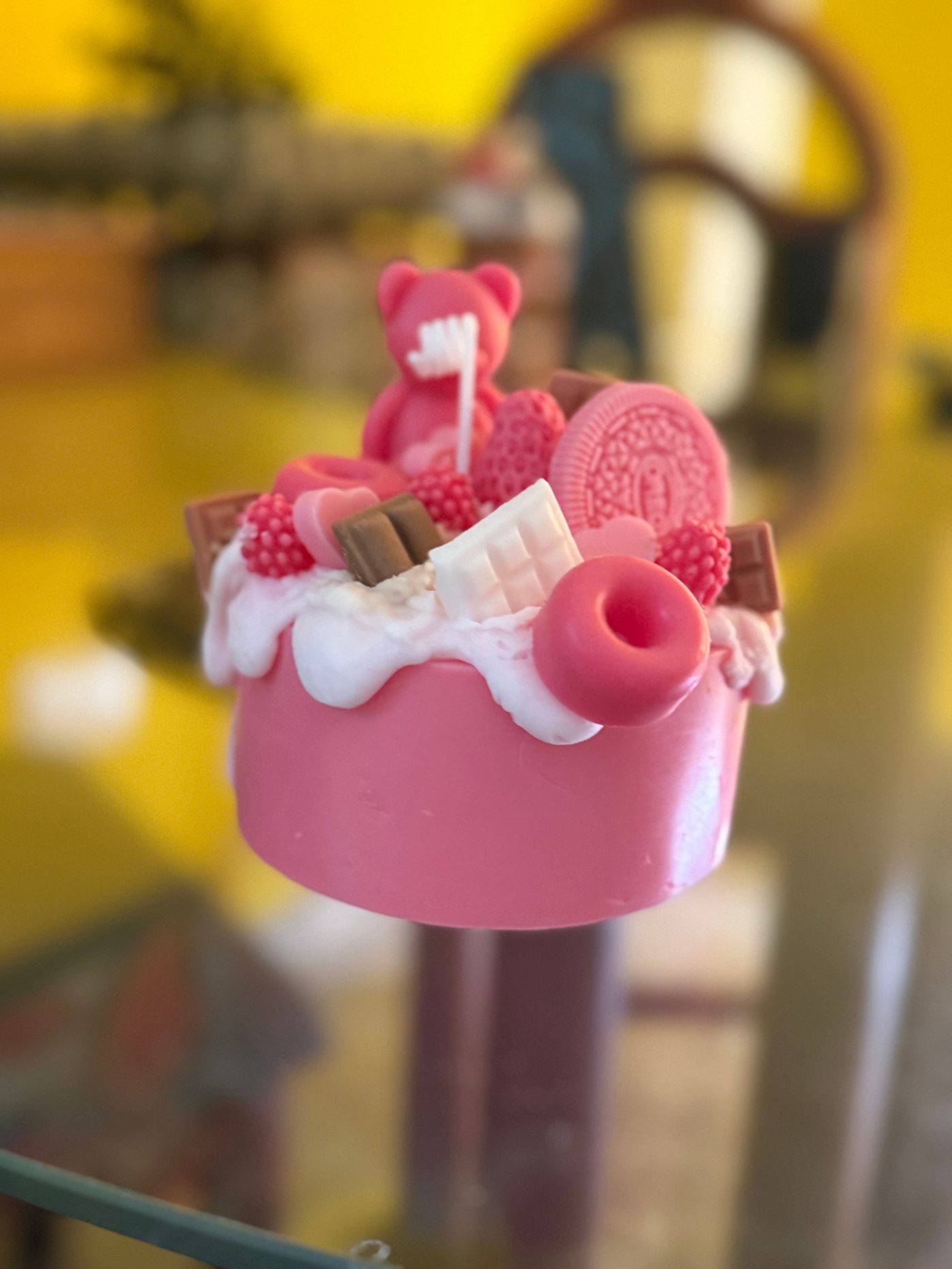 Vela artesanal tipo postre con forma de pastel y frutas en tonos coral y rosa.